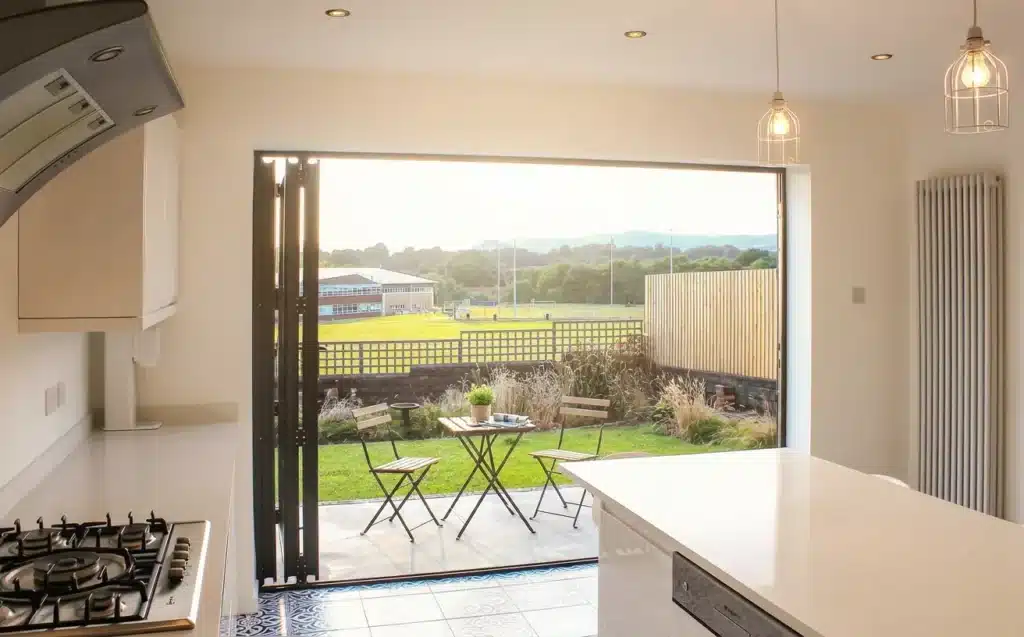 Open bi-fold doors connecting a bright kitchen to a summer backyard patio