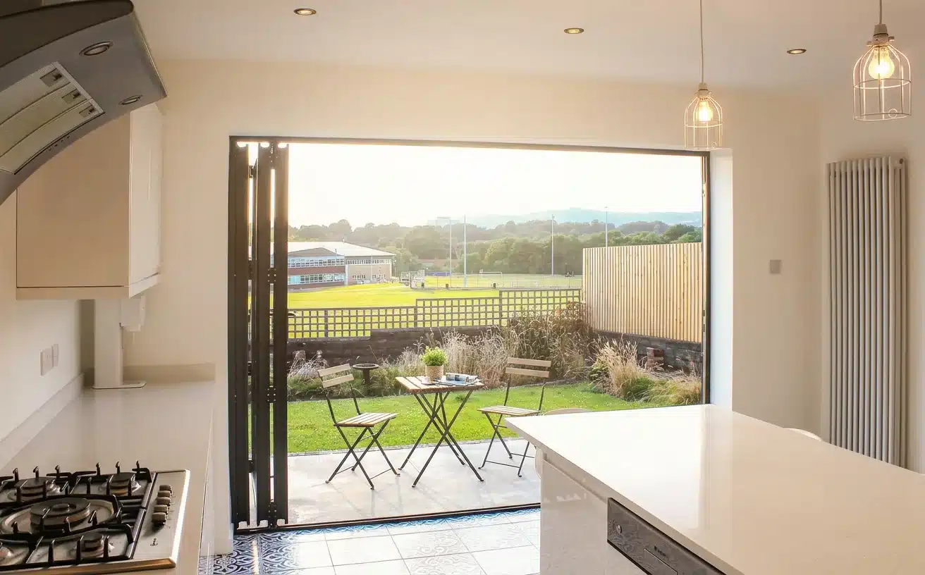Open bi-fold doors connecting a bright kitchen to a summer backyard patio