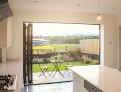 Open bi-fold doors connecting a bright kitchen to a summer backyard patio