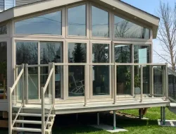 3-season glass sunroom installed on a raised backyard deck with visible footings and stairs