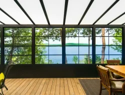 Dining table inside a Model 200 vinyl sunroom overlooking a green lakeside yard